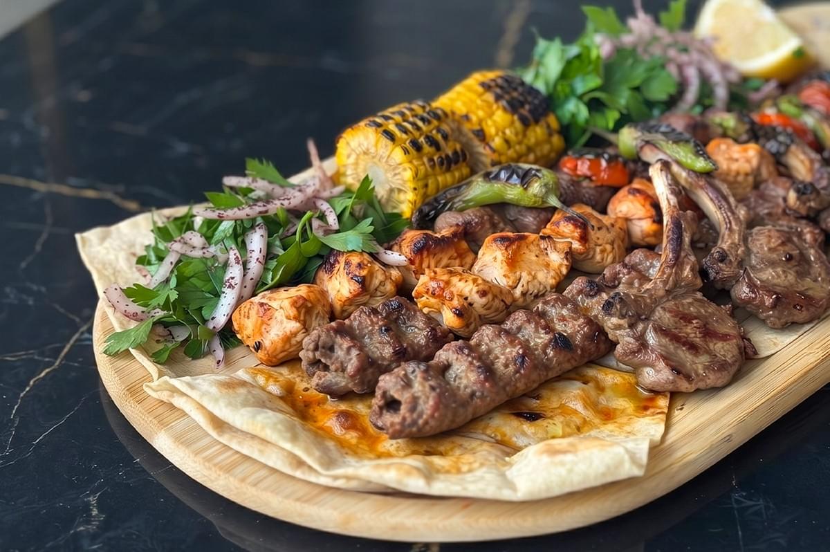 An authentic Turkish mixed grill platter featuring lamb chops, shish tawook, and Adana kebab, served with grilled corn, roasted peppers, and a fresh parsley salad on flatbread. An authentic Turkish mixed grill platter featuring lamb chops, shish tawook, and Adana kebab, served with grilled corn, roasted peppers, and a fresh parsley salad on flatbread.