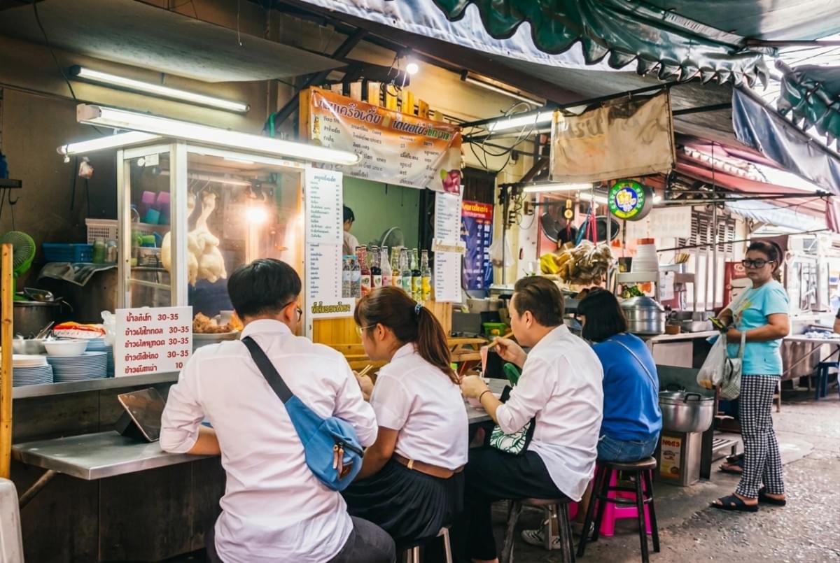 Customers seated on stools eating at an open-air food stall along a alleyway. Customers seated on stools eating at an open-air food stall along a alleyway.
