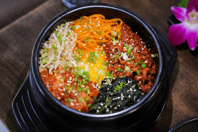 A sizzling dolsot bibimbap in a heavy black stone pot. This version features minced meat, radish salad, seaweed, and kimchi, with a raw egg yolk in the center ready to be mixed. The dish is garnished with fresh green onions and sesame seeds. A sizzling dolsot bibimbap in a heavy black stone pot. This version features minced meat, radish salad, seaweed, and kimchi, with a raw egg yolk in the center ready to be mixed. The dish is garnished with fresh green onions and sesame seeds.