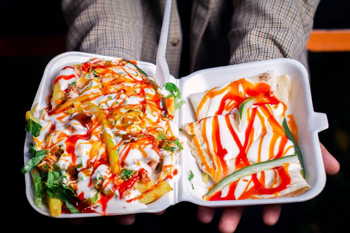 Person holding a takeout container of affordable halal street food drizzled with sauce. Person holding a takeout container of affordable halal street food drizzled with sauce.