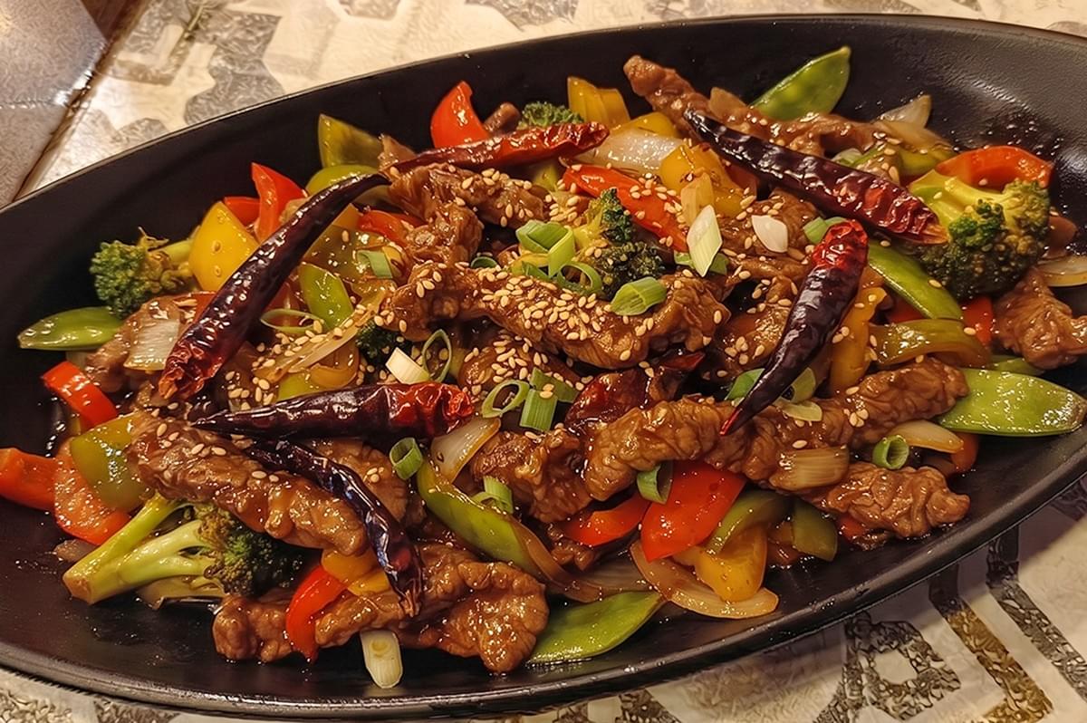 Spicy beef with dried chili, vegetables, and sesame seeds served in a black plate. Spicy beef with dried chili, vegetables, and sesame seeds served in a black plate.