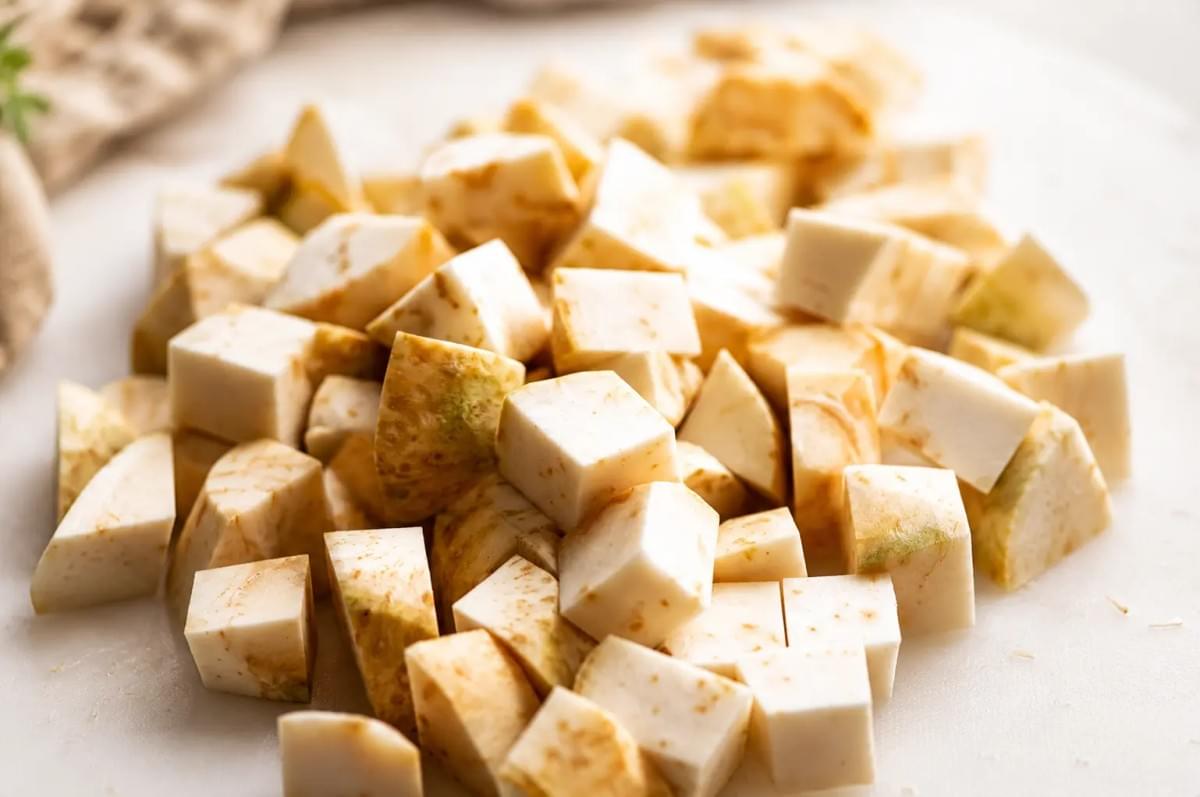 A pile of raw, finely diced celeriac root cubes on a cutting surface. A pile of raw, finely diced celeriac root cubes on a cutting surface.