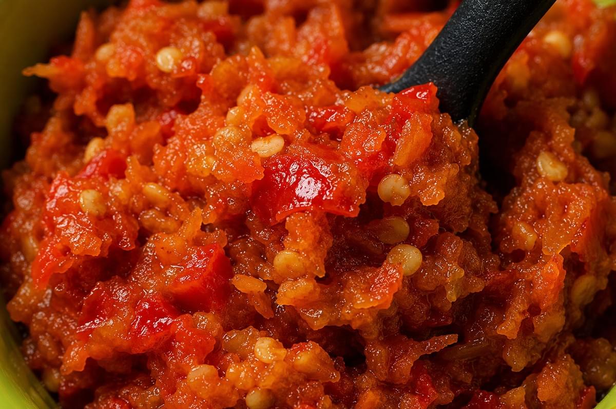 Close-up view of chunky red sambal chili paste with visible seeds and black serving spoon Close-up view of chunky red sambal chili paste with visible seeds and black serving spoon