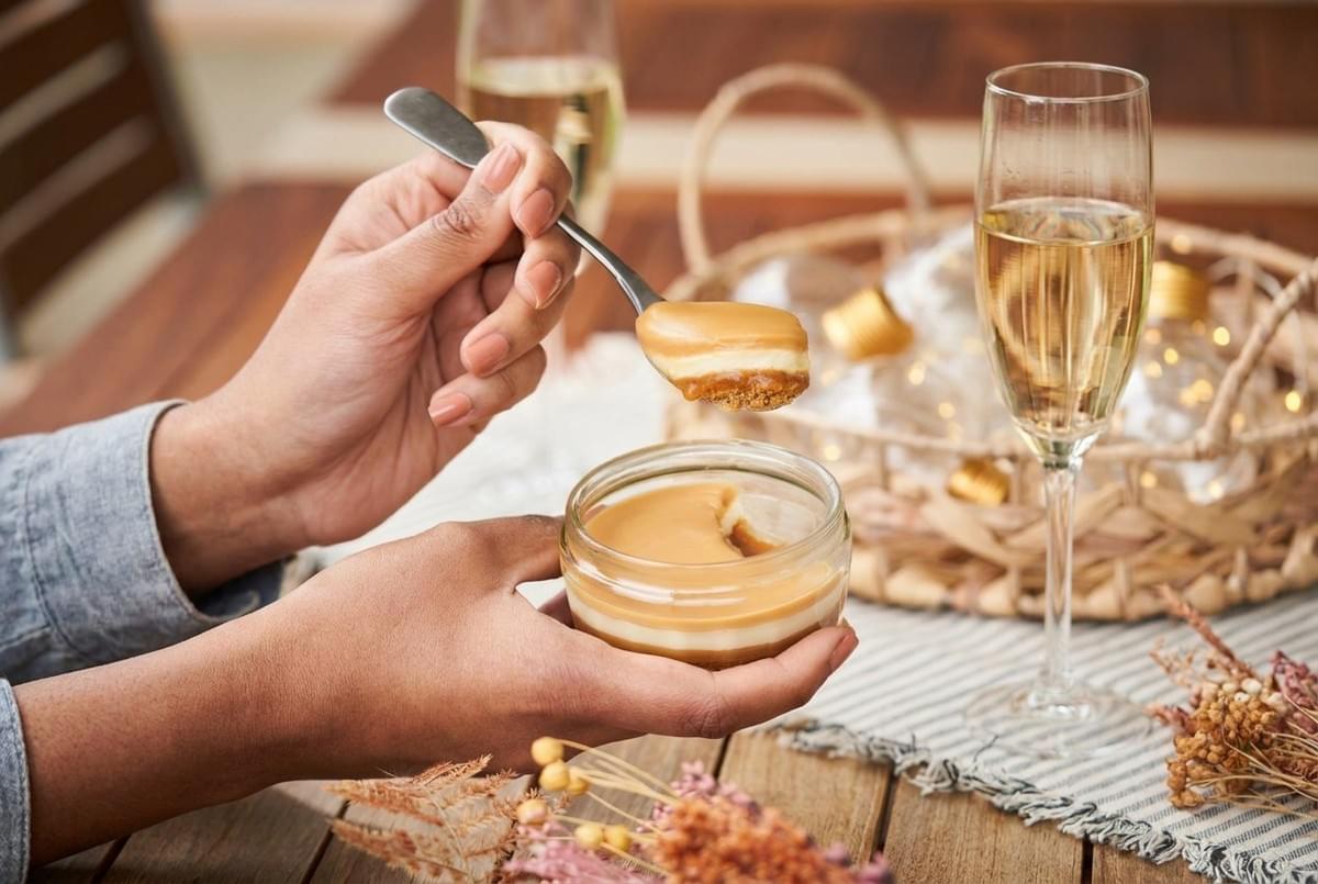 Hand holding a spoon dipping into a glass jar filled with layered caramel dessert. Hand holding a spoon dipping into a glass jar filled with layered caramel dessert.