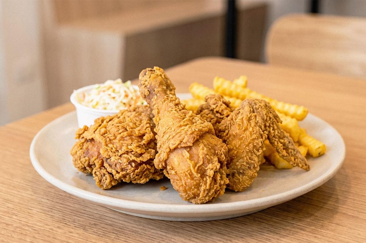 Crispy fried chicken pieces served with crinkle-cut fries and a side of creamy coleslaw on a white plate. Crispy fried chicken pieces served with crinkle-cut fries and a side of creamy coleslaw on a white plate.