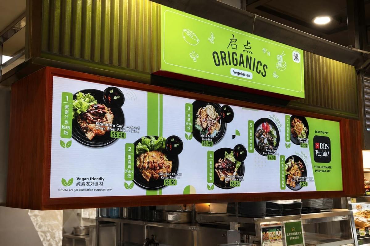 Origanics Vegetarian hawker stall featuring a bright green sign and a digital menu board displaying vegan-friendly rice dishes Origanics Vegetarian hawker stall featuring a bright green sign and a digital menu board displaying vegan-friendly rice dishes