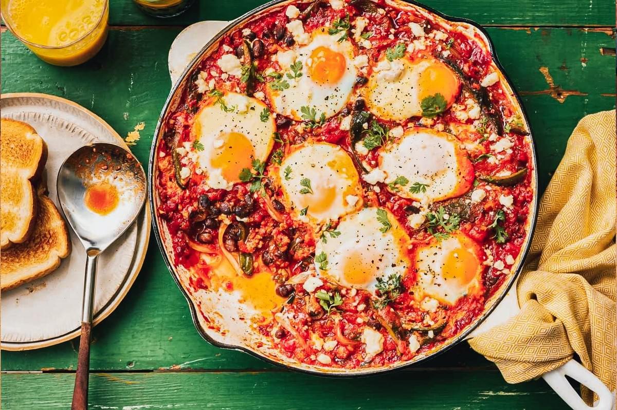 Overhead shot of huevos rancheros with fried eggs on a rich tomato chili sauce, topped with herbs and cheese, served with toast and juice for a vibrant Mexican breakfast Overhead shot of huevos rancheros with fried eggs on a rich tomato chili sauce, topped with herbs and cheese, served with toast and juice for a vibrant Mexican breakfast