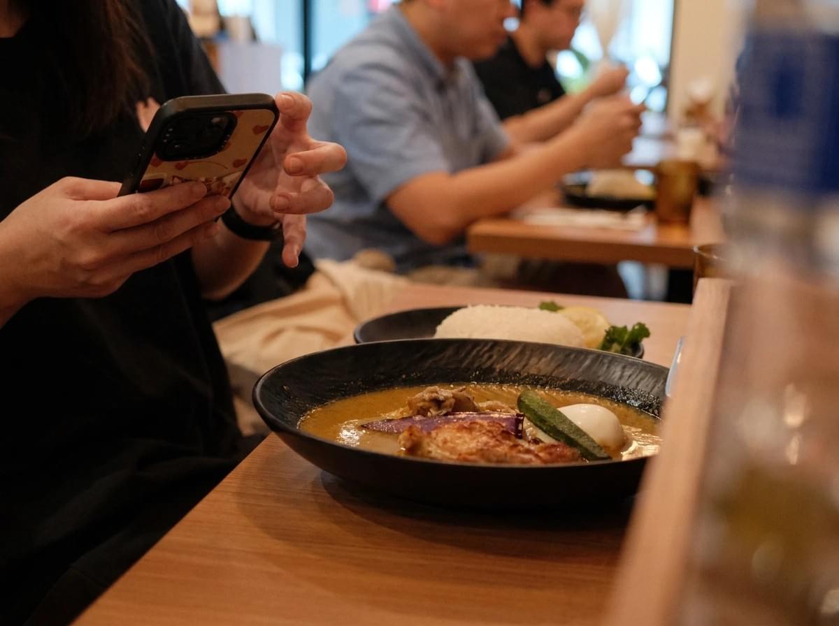 Person taking a smartphone photo of a bowl of soup curry at a restaurant table. Person taking a smartphone photo of a bowl of soup curry at a restaurant table.