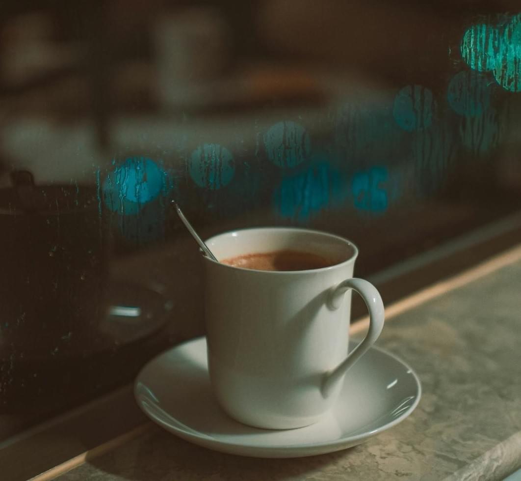 Cozy scene of a hot cup of coffee by a rainy window with blurred city bokeh in the background. Cozy scene of a hot cup of coffee by a rainy window with blurred city bokeh in the background.