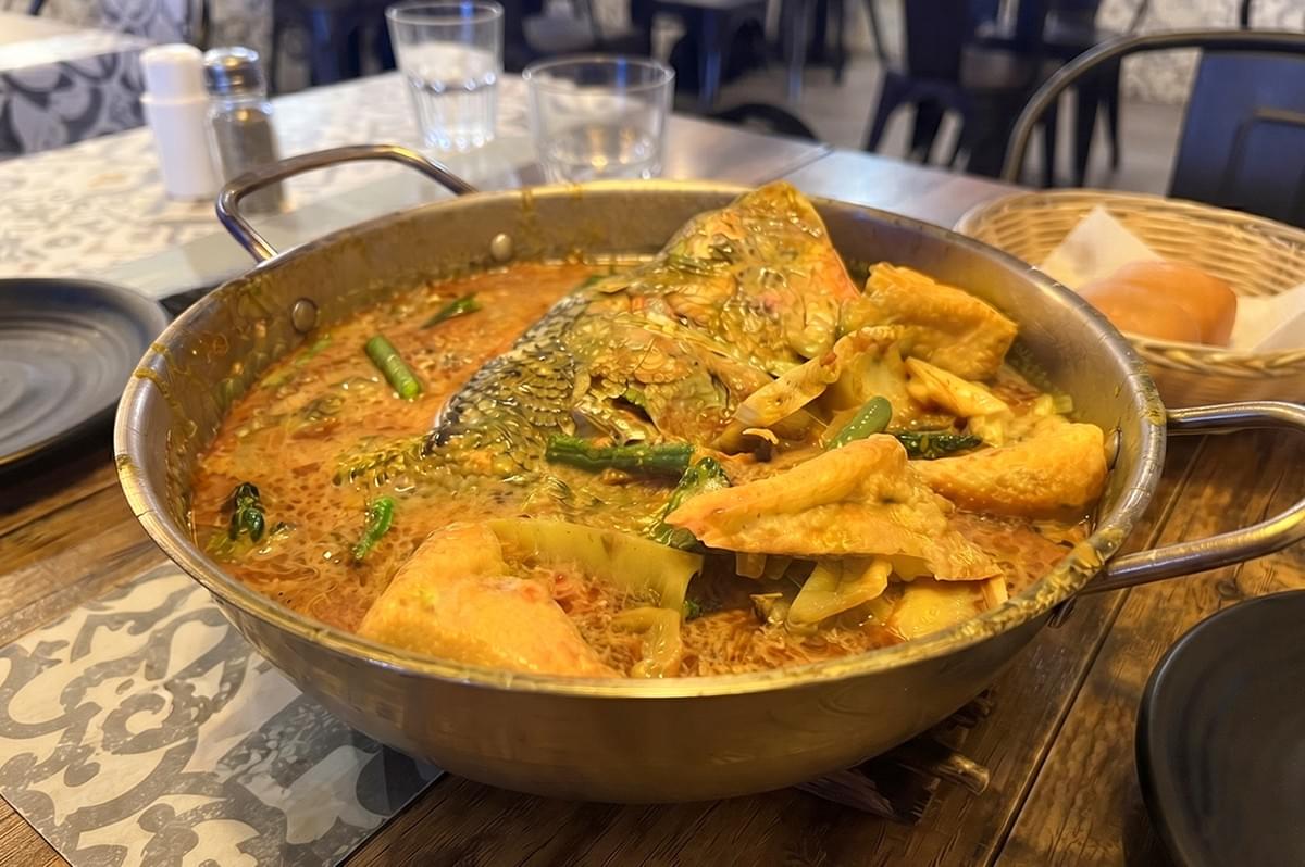Delicious traditional curry fish head served in a metal pot at a restaurant. Delicious traditional curry fish head served in a metal pot at a restaurant.
