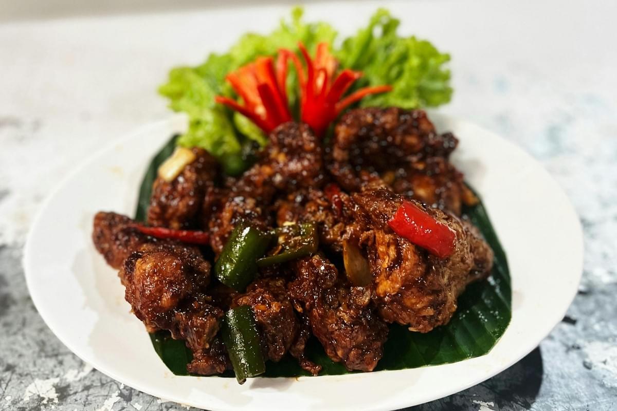 In the image, a plate of savory, dark-sauced stir-fried meat is served over a green banana leaf on a white plate. The dish is garnished with chopped green and red chili peppers, fresh lettuce, and a decorative red chili flower in the background. In the image, a plate of savory, dark-sauced stir-fried meat is served over a green banana leaf on a white plate. The dish is garnished with chopped green and red chili peppers, fresh lettuce, and a decorative red chili flower in the background.