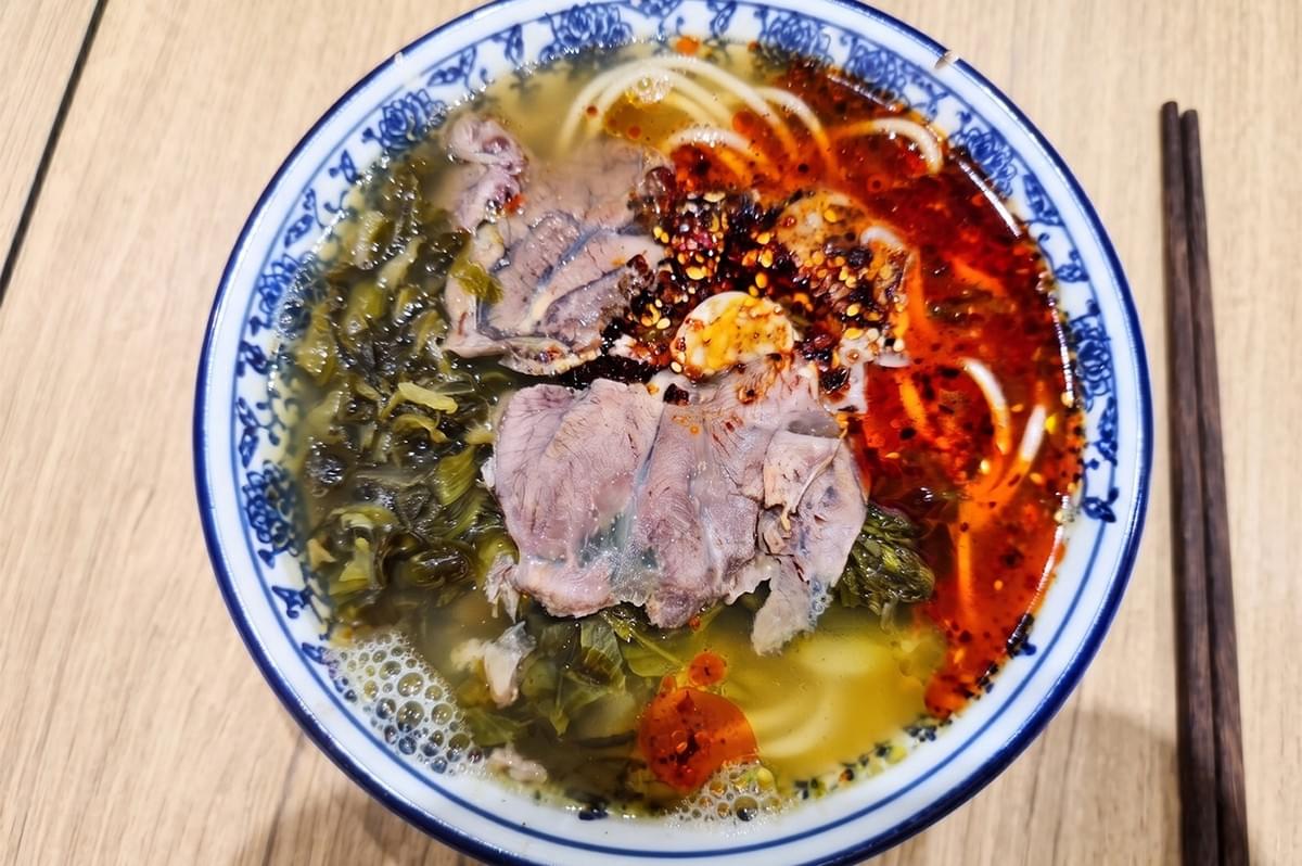 Bowl of Tongue Tip hand-pulled beef noodles topped with sliced beef, pickled vegetables, and chili oil. Bowl of Tongue Tip hand-pulled beef noodles topped with sliced beef, pickled vegetables, and chili oil.