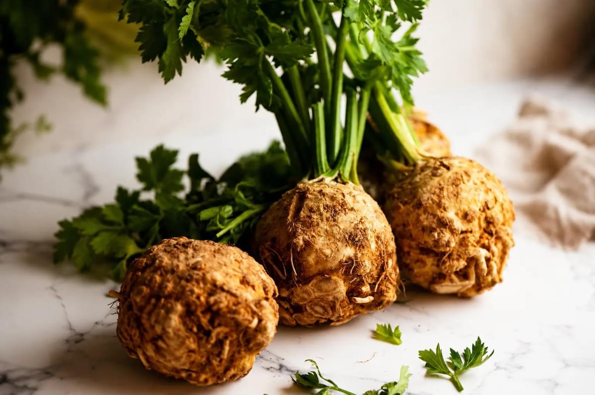 Whole celeriac roots with green leafy stalks resting on a marble countertop. Whole celeriac roots with green leafy stalks resting on a marble countertop.