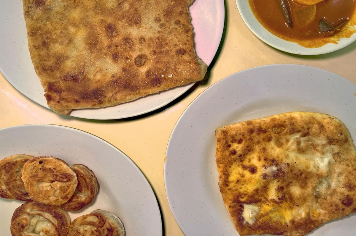 Plates of Malaysian Indian food are pictured, featuring roti canai and murtabak, with a side of curry. The scene suggests a warm, inviting meal. Plates of Malaysian Indian food are pictured, featuring roti canai and murtabak, with a side of curry. The scene suggests a warm, inviting meal.