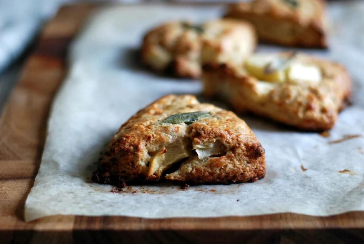 Close-up of a golden baked savory scone topped with a fresh sage leaf resting on parchment paper. Close-up of a golden baked savory scone topped with a fresh sage leaf resting on parchment paper.