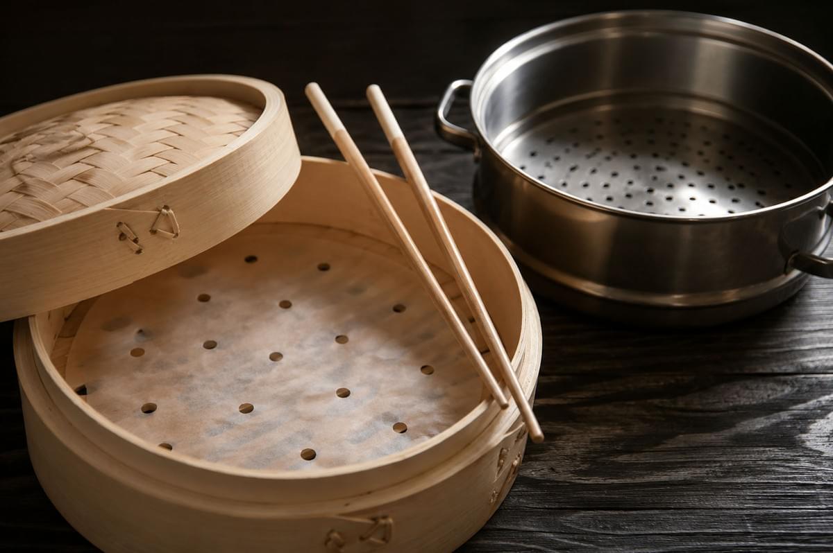 Bamboo steamer basket with chopsticks and a stainless steel steamer pot arranged on a dark wooden table Bamboo steamer basket with chopsticks and a stainless steel steamer pot arranged on a dark wooden table