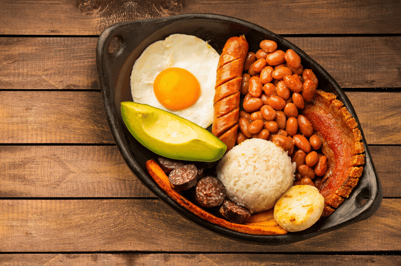 A meticulously arranged Bandeja Paisa in an oval clay dish, highlighting the contrast between the bright yellow egg yolk, the green avocado, and the deep textures of the fried meats and beans. A meticulously arranged Bandeja Paisa in an oval clay dish, highlighting the contrast between the bright yellow egg yolk, the green avocado, and the deep textures of the fried meats and beans.