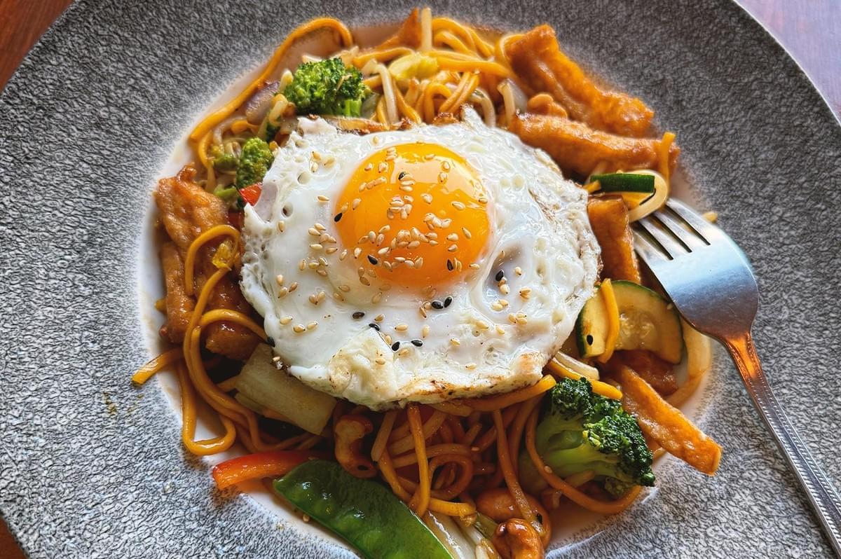 Top view of Mee Goreng with fried egg, brocolli, cucumber and pork meat topped with sesame seeds Top view of Mee Goreng with fried egg, brocolli, cucumber and pork meat topped with sesame seeds