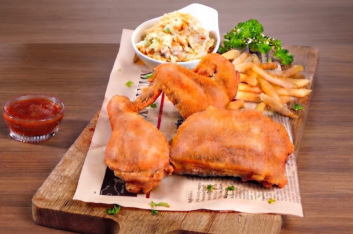 Crispy fried chicken platter with fries, coleslaw, and dipping sauce on a wooden board with paper. Crispy fried chicken platter with fries, coleslaw, and dipping sauce on a wooden board with paper.