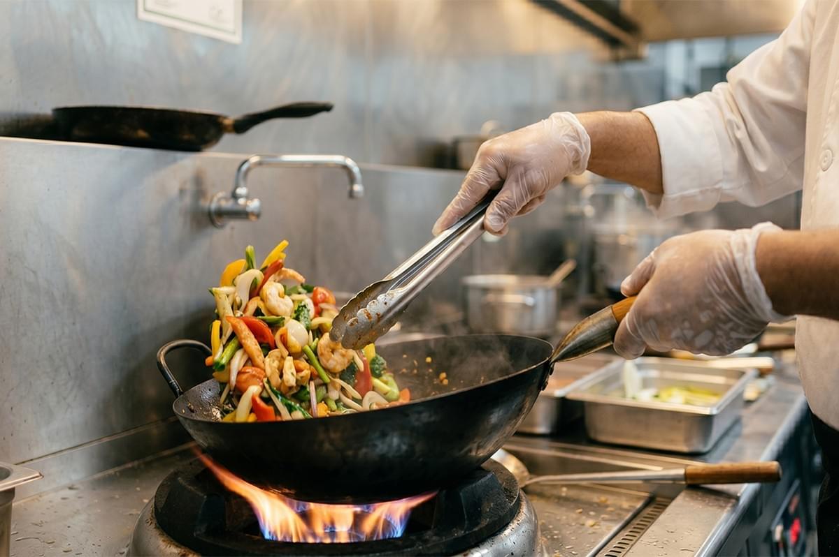 Chef cooking a colorful shrimp and vegetable stir-fry in a wok over an open gas flame. Chef cooking a colorful shrimp and vegetable stir-fry in a wok over an open gas flame.
