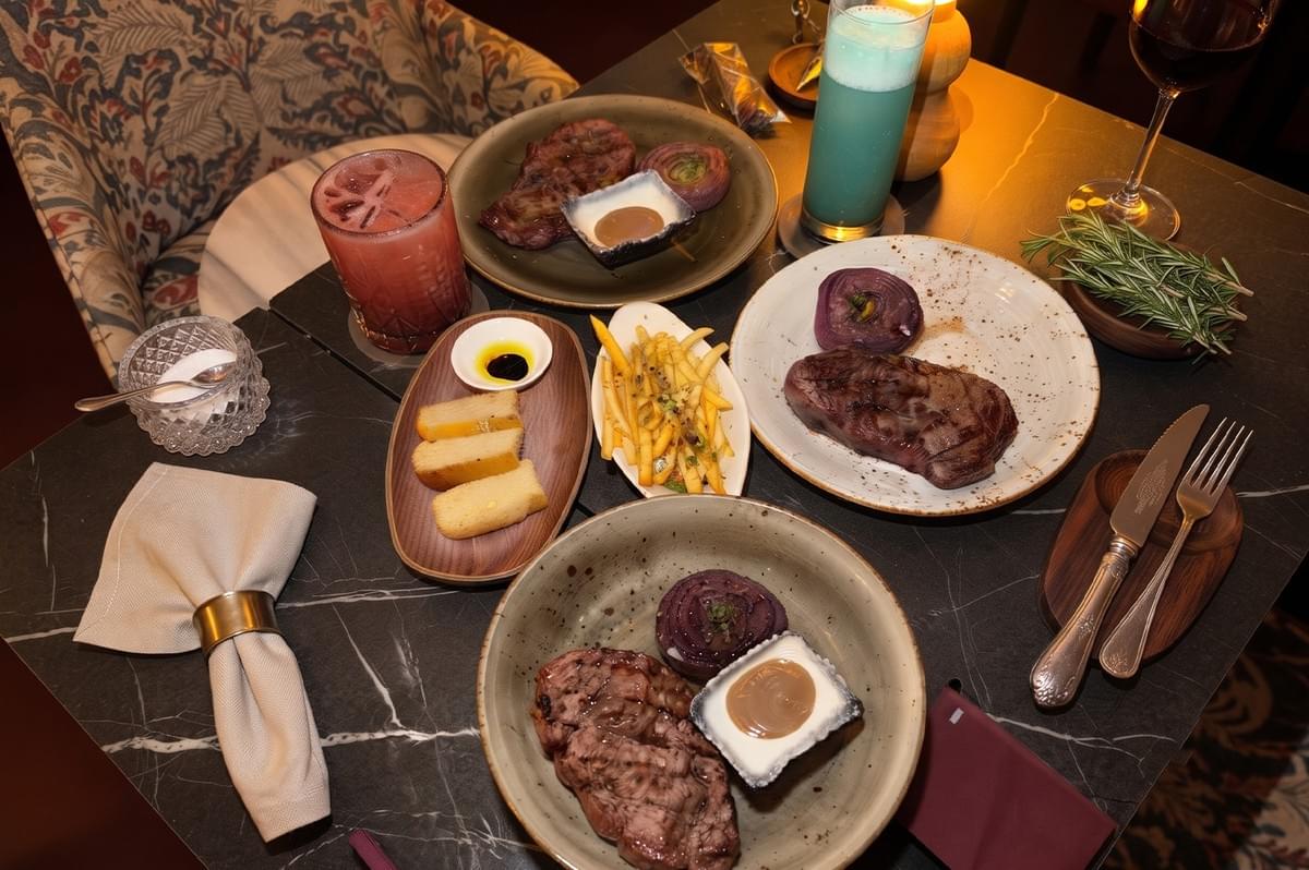 Gourmet dining table spread with wagyu striploin, steaks, fries, and colorful cocktails. Gourmet dining table spread with wagyu striploin, steaks, fries, and colorful cocktails.
