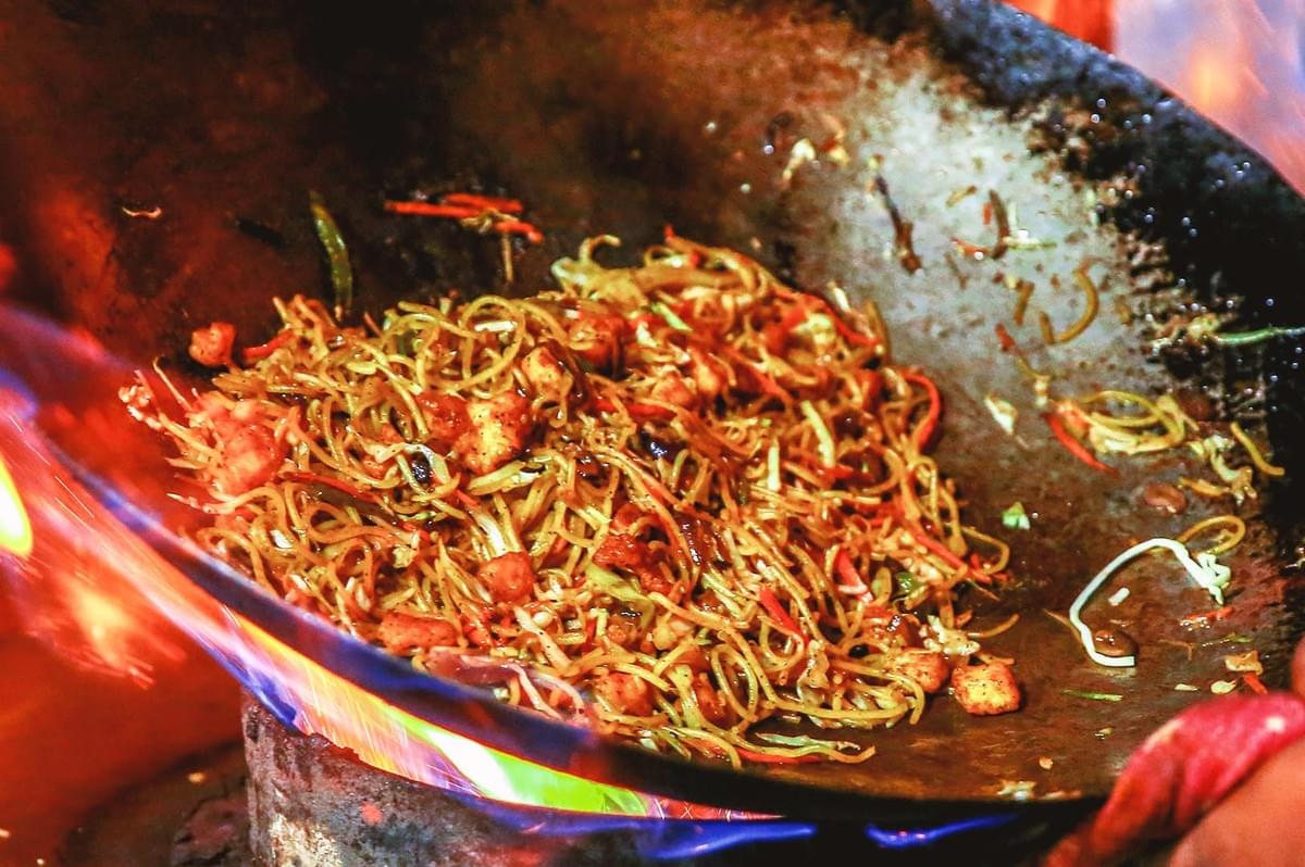 Close up of spicy noodles being sauteed in huge black wok in high heat Close up of spicy noodles being sauteed in huge black wok in high heat