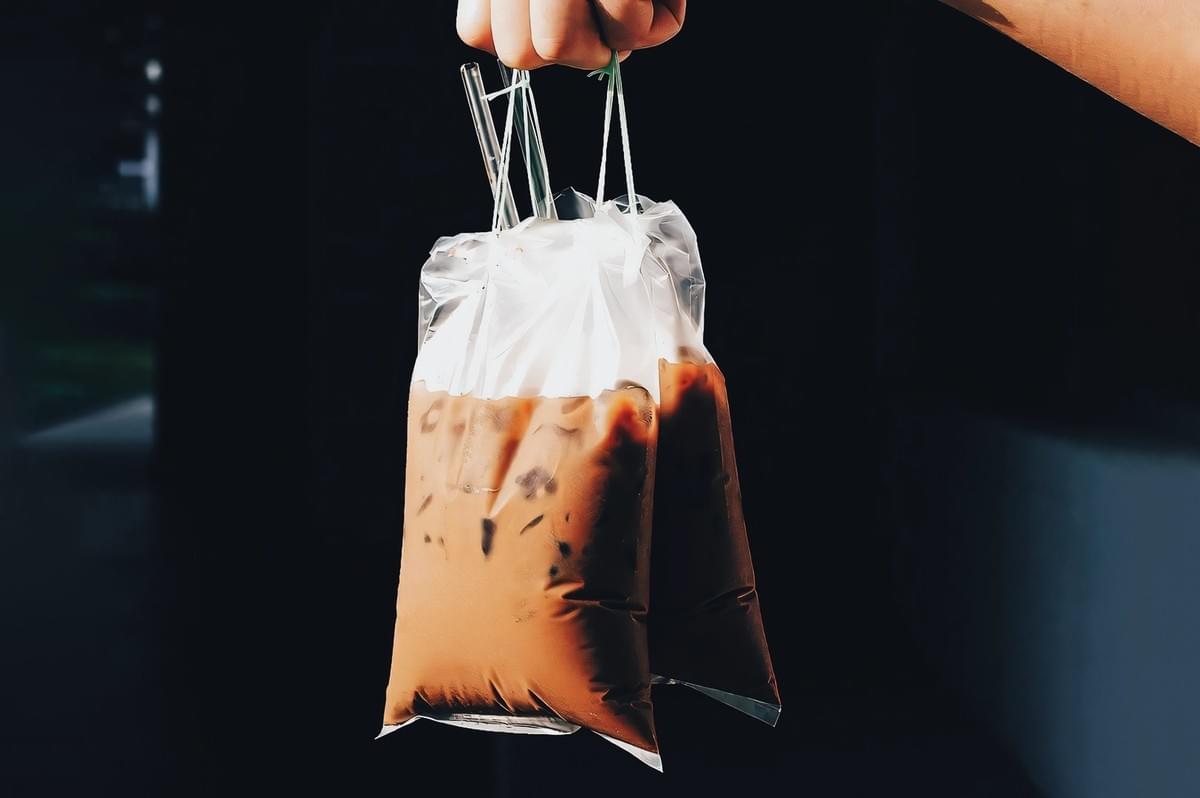 Close-up eye-level shot of takeaway Singapore kopi tied in plastic bags, a common local coffee tradition at hawker centres and kopitiams. Close-up eye-level shot of takeaway Singapore kopi tied in plastic bags, a common local coffee tradition at hawker centres and kopitiams.