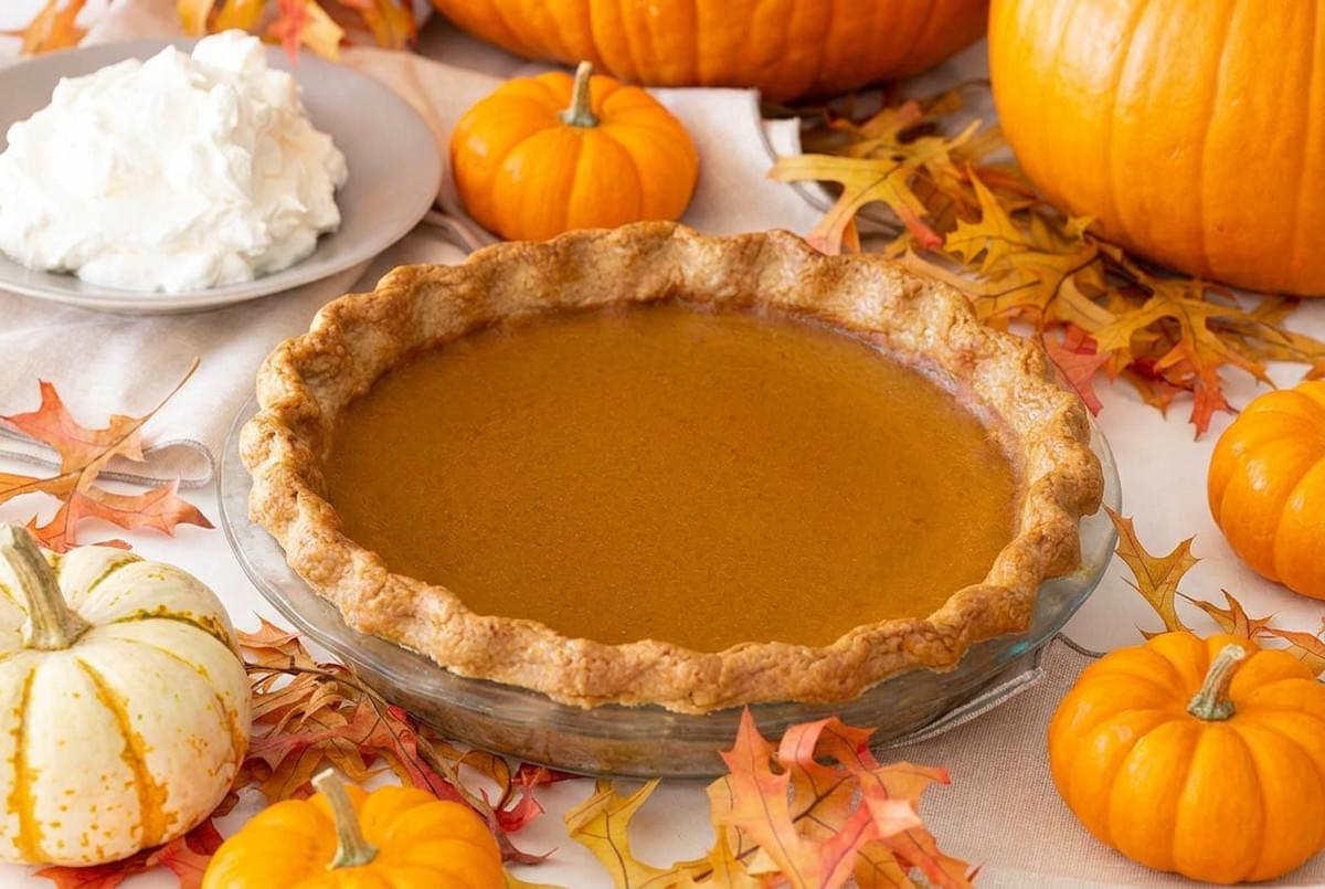 Whole freshly baked pumpkin pie surrounded by mini pumpkins and autumn leaves. Whole freshly baked pumpkin pie surrounded by mini pumpkins and autumn leaves.