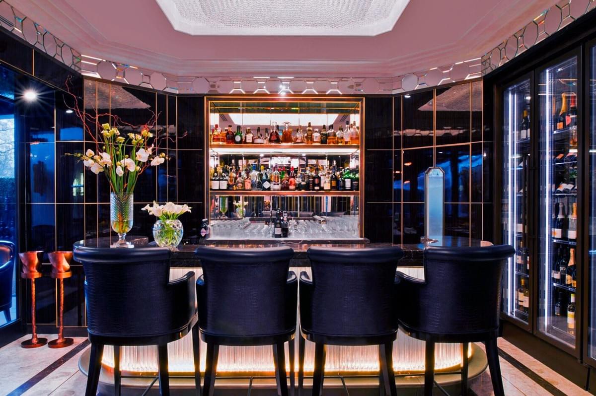 Luxurious home bar with black chairs and backlit shelves filled with bottles. Elegant decor features flowers and soft lighting, conveying a sophisticated ambiance. Luxurious home bar with black chairs and backlit shelves filled with bottles. Elegant decor features flowers and soft lighting, conveying a sophisticated ambiance.