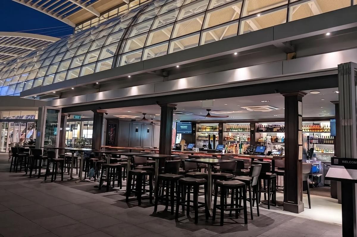 Dallas Cafe outdoor bar with high-top tables and stools under a modern glass dome roof structure. Dallas Cafe outdoor bar with high-top tables and stools under a modern glass dome roof structure.