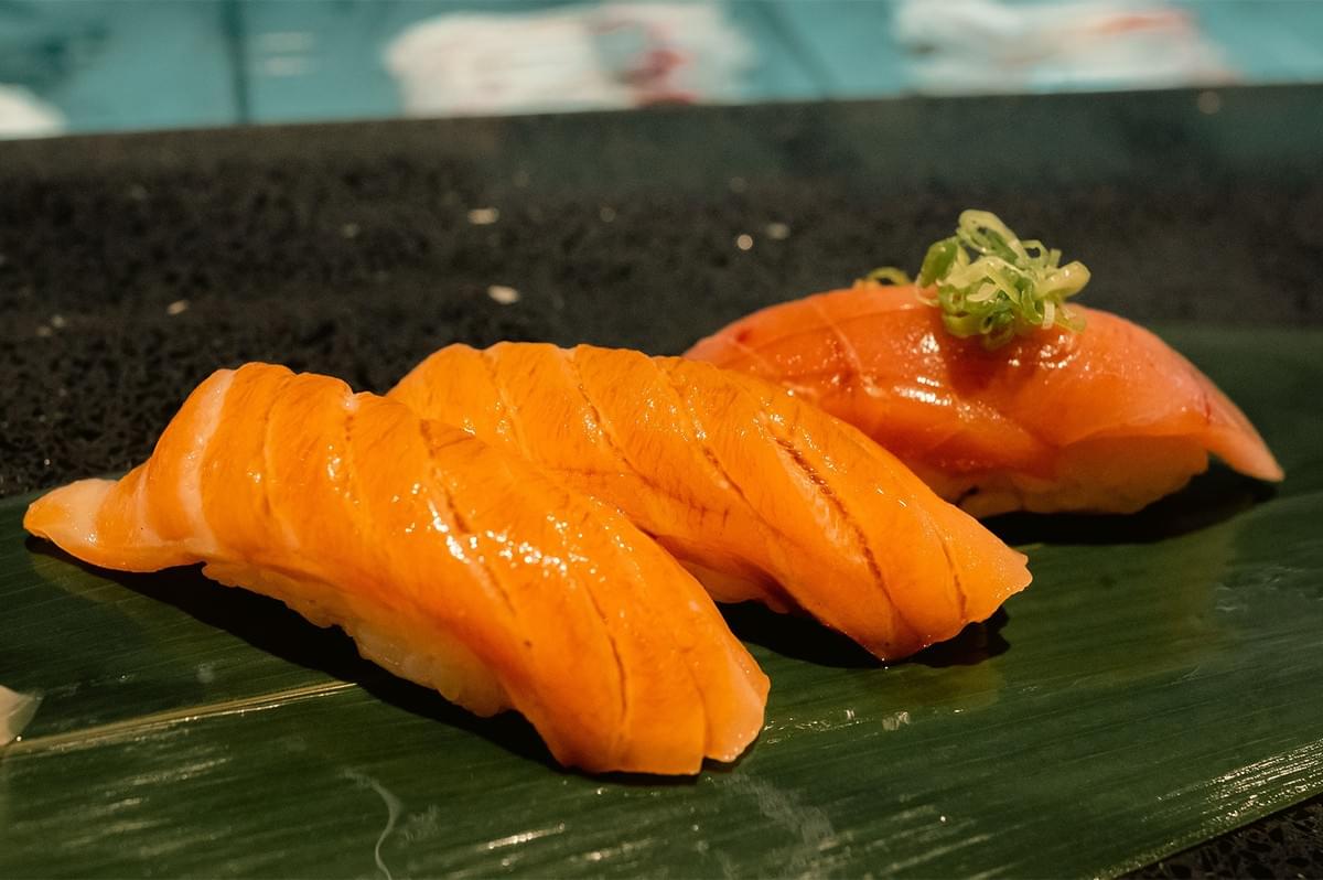 Close-up of fresh salmon nigiri and torched aburi sushi served on a banana leaf at a Shabu-Sushi buffet. Close-up of fresh salmon nigiri and torched aburi sushi served on a banana leaf at a Shabu-Sushi buffet.
