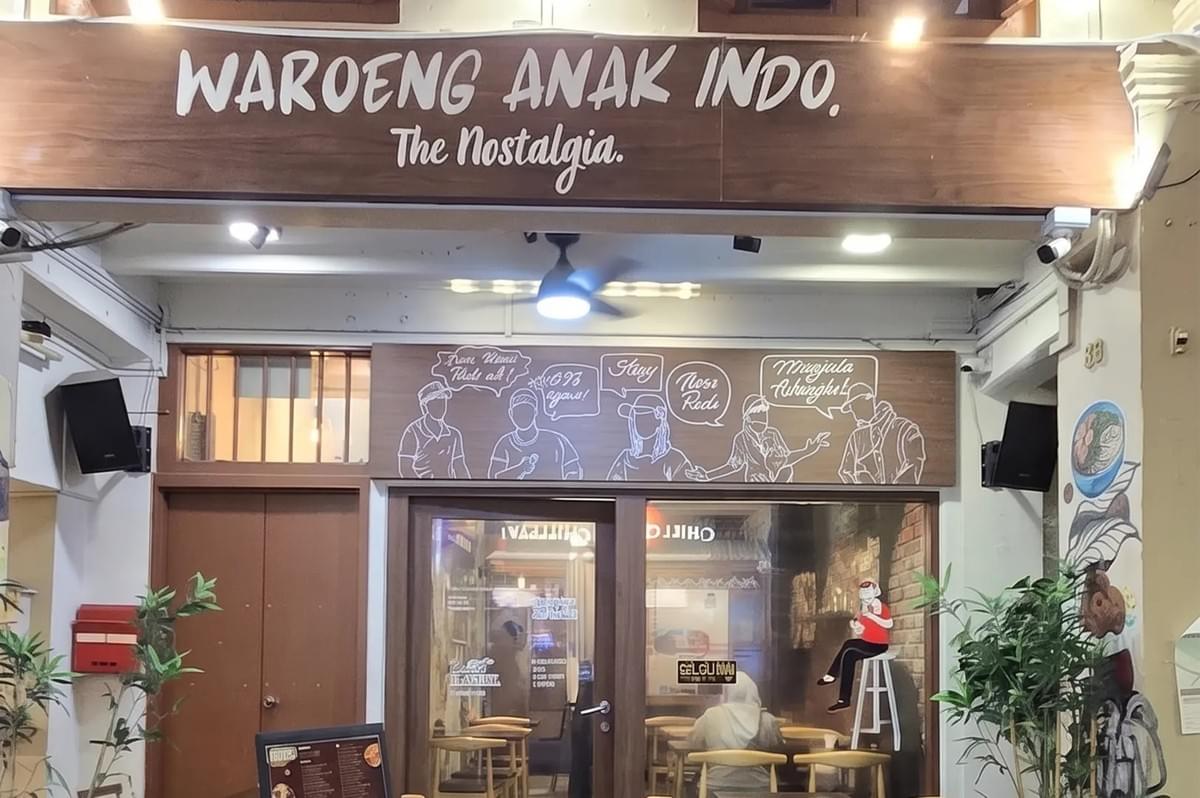 Storefront of Waroeng Anak Indo restaurant with illustrated window graphics and a wooden sign. Storefront of Waroeng Anak Indo restaurant with illustrated window graphics and a wooden sign.