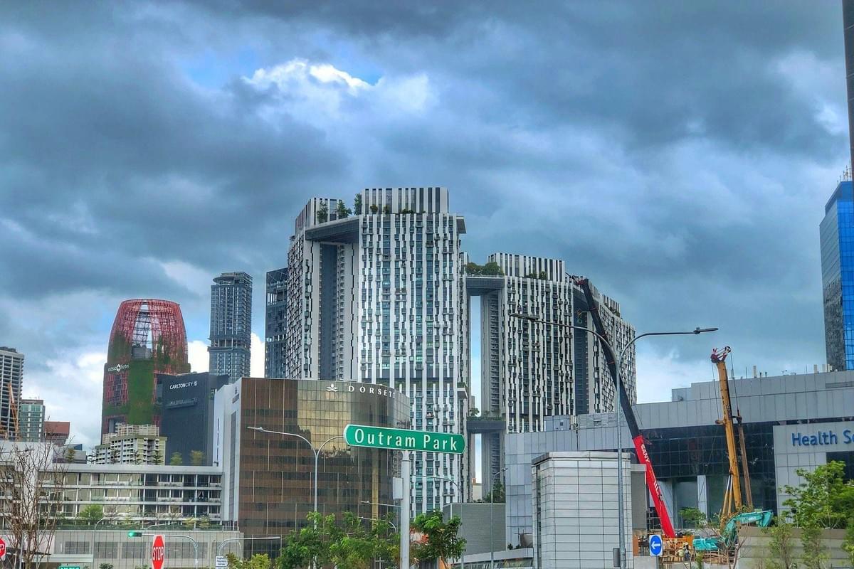 The image showcases the urban skyline of Outram, Singapore, featuring the iconic Pinnacle Duxton residential towers and the distinctive red, greenery-covered Oasia Hotel Downtown. A green street sign for Outram Park stands in the foreground under a dramatic, cloudy sky. The image showcases the urban skyline of Outram, Singapore, featuring the iconic Pinnacle Duxton residential towers and the distinctive red, greenery-covered Oasia Hotel Downtown. A green street sign for Outram Park stands in the foreground under a dramatic, cloudy sky.