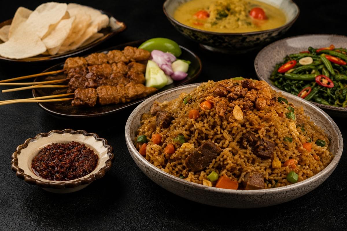 Indonesian meal spread featuring nasi goreng fried rice, satay skewers, crackers, vegetables, and sambal condiment Indonesian meal spread featuring nasi goreng fried rice, satay skewers, crackers, vegetables, and sambal condiment