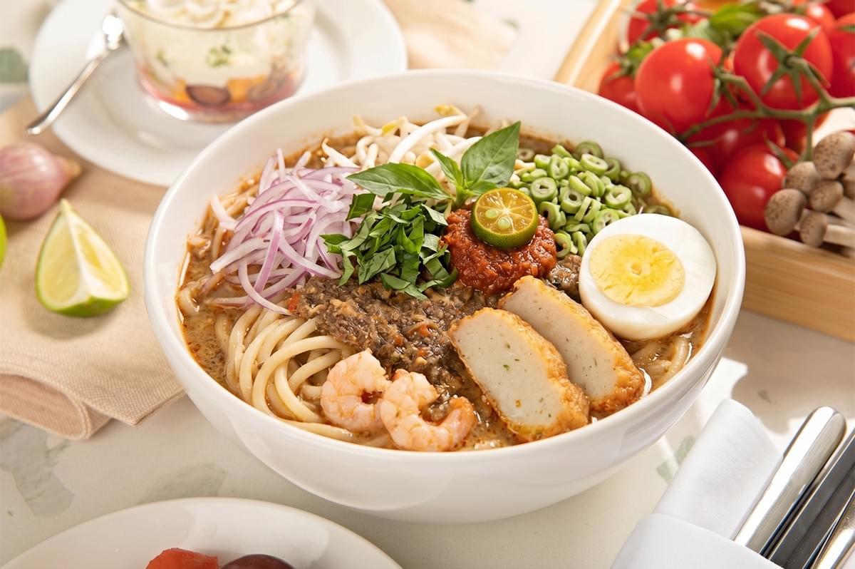 A bowl of laksa noodle soup topped with prawns, fish cakes, hard-boiled egg, and fresh herbs. A bowl of laksa noodle soup topped with prawns, fish cakes, hard-boiled egg, and fresh herbs.