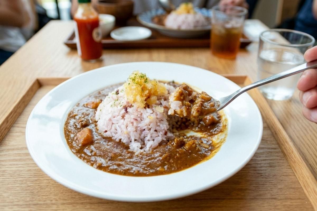 Spoon lifting a bite of curry and rice from a white plate served on a wooden tray at a cafe Spoon lifting a bite of curry and rice from a white plate served on a wooden tray at a cafe