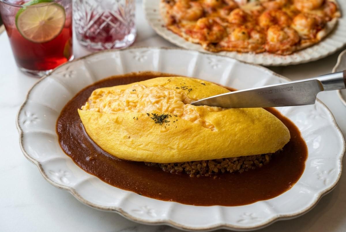 A knife cutting into a classic Japanese omelet placed over fried rice and dark gravy. A knife cutting into a classic Japanese omelet placed over fried rice and dark gravy.