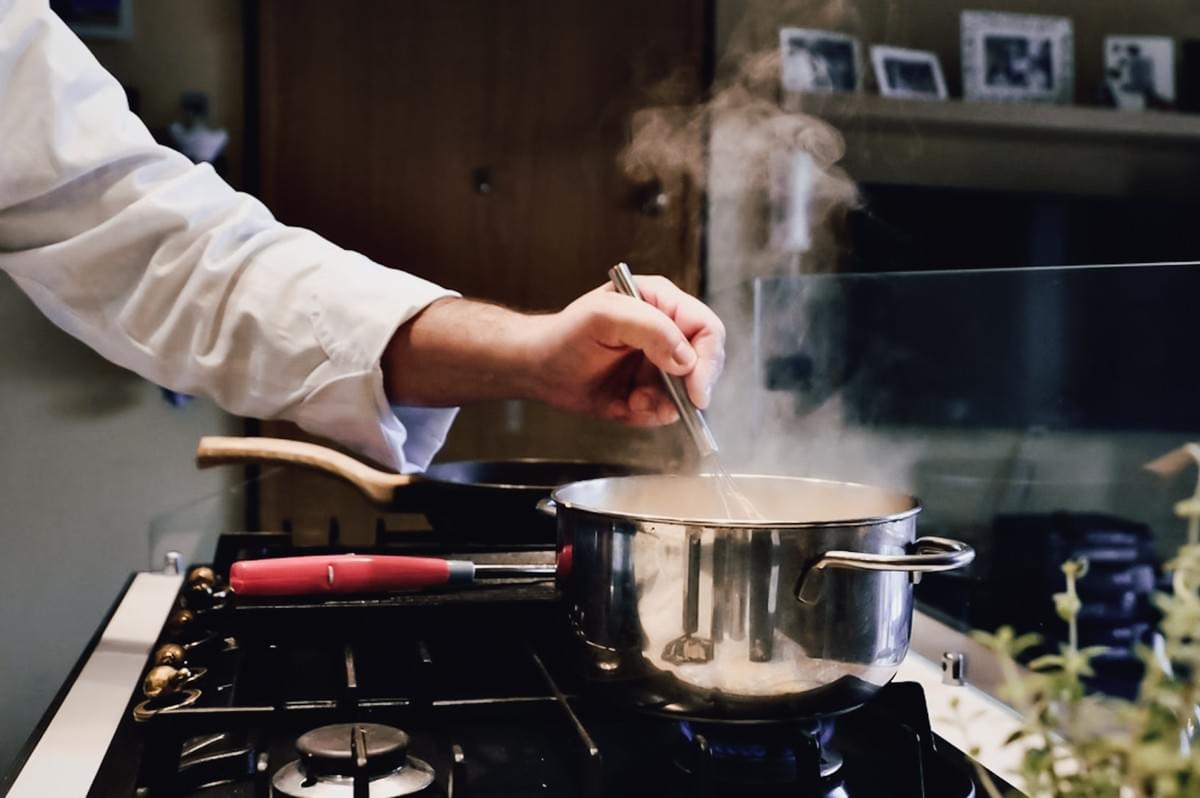 Eye-level close-up shot of hand whisking steaming pot on stovetop, capturing preparation of rich German comfort food sauce in a tropical kitchen, highlighting expat cooking in humid climate Eye-level close-up shot of hand whisking steaming pot on stovetop, capturing preparation of rich German comfort food sauce in a tropical kitchen, highlighting expat cooking in humid climate