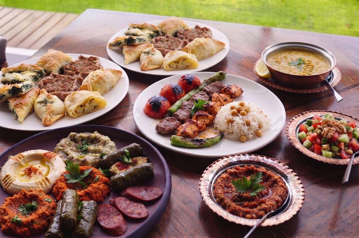 Spread of Middle Eastern cuisine including kebabs, rice, hummus, dolmas, and assorted pastries on a wooden table. Spread of Middle Eastern cuisine including kebabs, rice, hummus, dolmas, and assorted pastries on a wooden table.