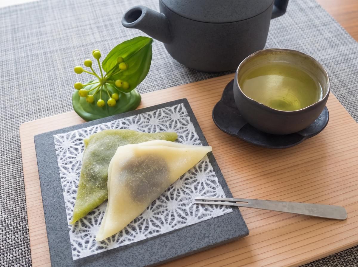 Green matcha and original yatsuhashi served on a stone plate alongside a teacup and teapot. Green matcha and original yatsuhashi served on a stone plate alongside a teacup and teapot.