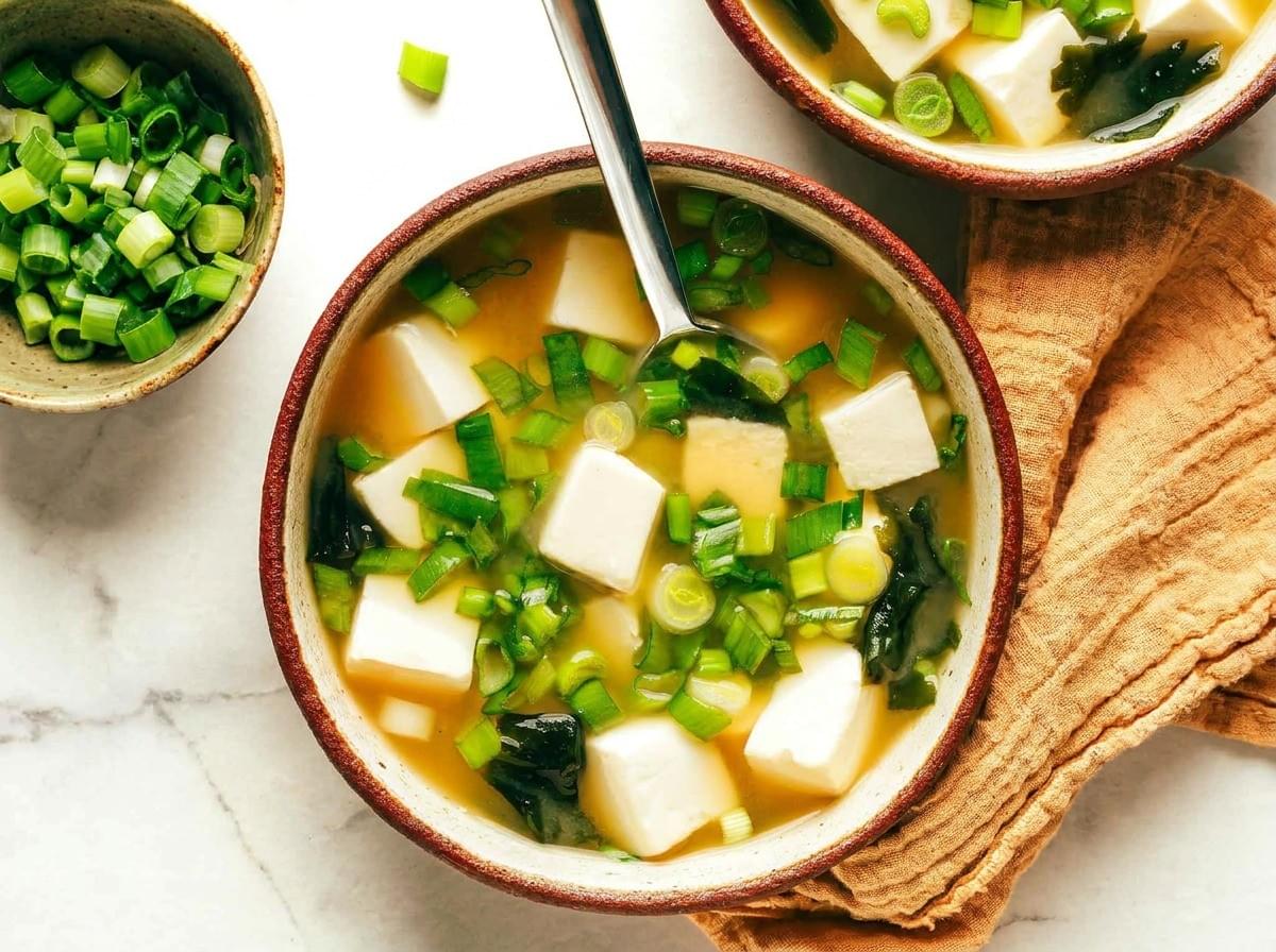 Top-down view of a bowl of miso soup packed with tofu cubes and sliced green onions. Top-down view of a bowl of miso soup packed with tofu cubes and sliced green onions.