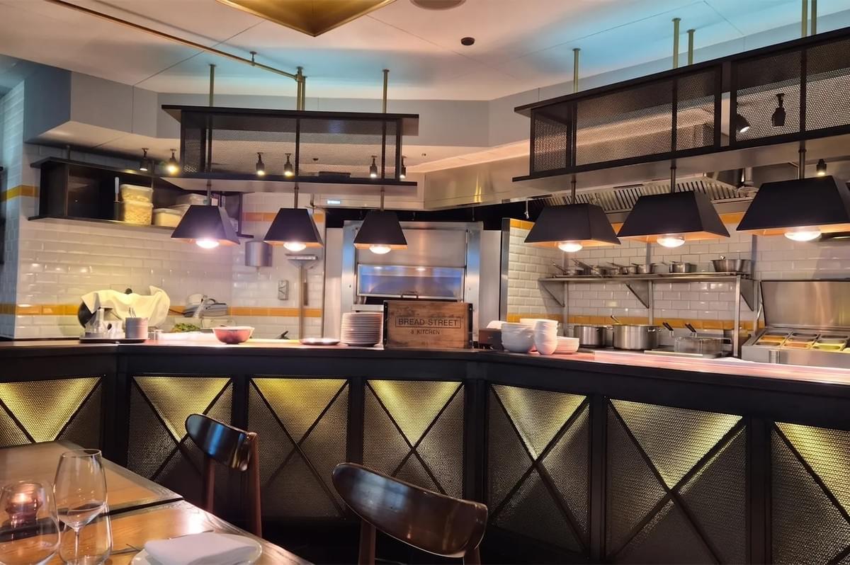 Bread Street Kitchen restaurant interior showing an open kitchen counter with hanging pendant lights. Bread Street Kitchen restaurant interior showing an open kitchen counter with hanging pendant lights.