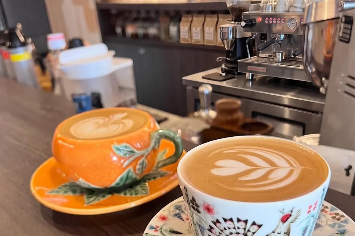 Two cups of latte with heart latte art on a wooden cafe counter next to an espresso machine. Two cups of latte with heart latte art on a wooden cafe counter next to an espresso machine.