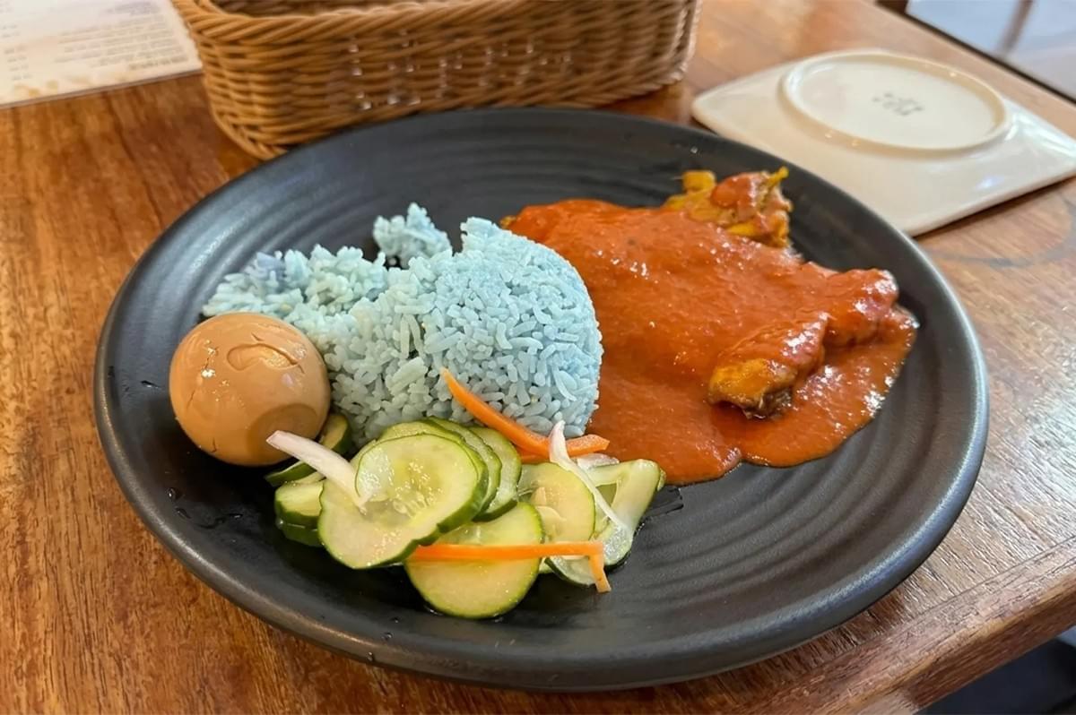 Nasi Kerabu featuring blue pea flower rice, chicken in red curry sauce, a salted egg, and fresh cucumber salad. Nasi Kerabu featuring blue pea flower rice, chicken in red curry sauce, a salted egg, and fresh cucumber salad.
