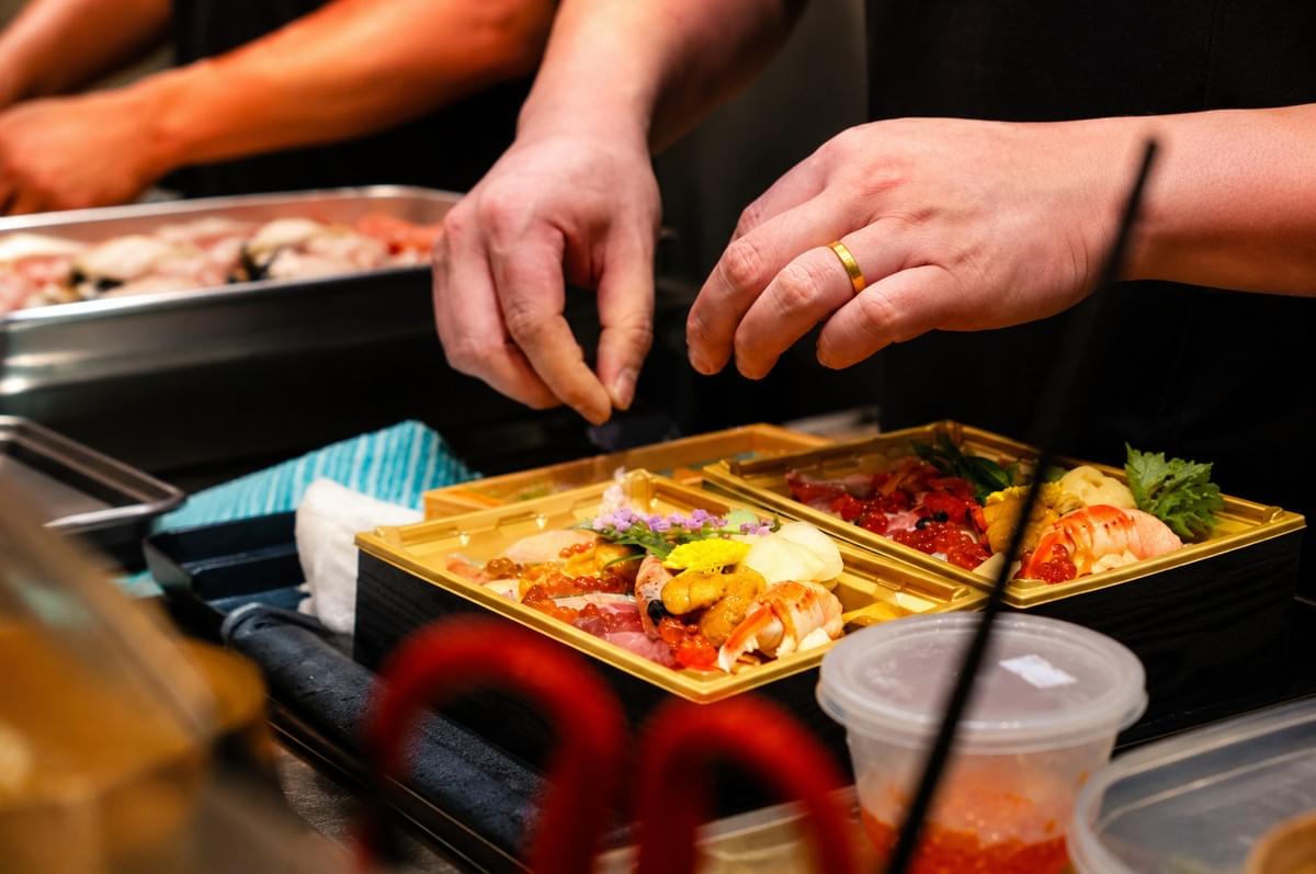 Chef carefully arranging fresh ingredients on a premium chirashi bento box. Chef carefully arranging fresh ingredients on a premium chirashi bento box.