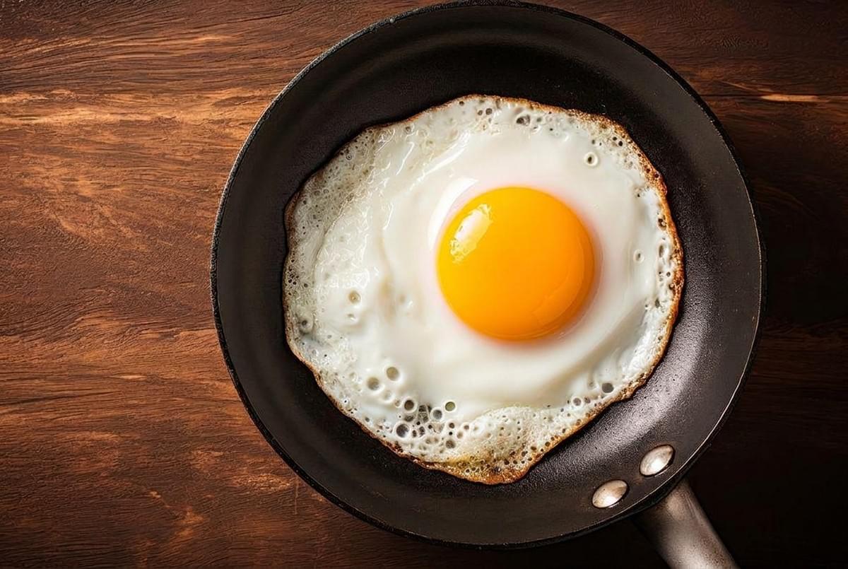 Sunny-side-up egg with a bright yellow yolk frying in a black skillet. Sunny-side-up egg with a bright yellow yolk frying in a black skillet.