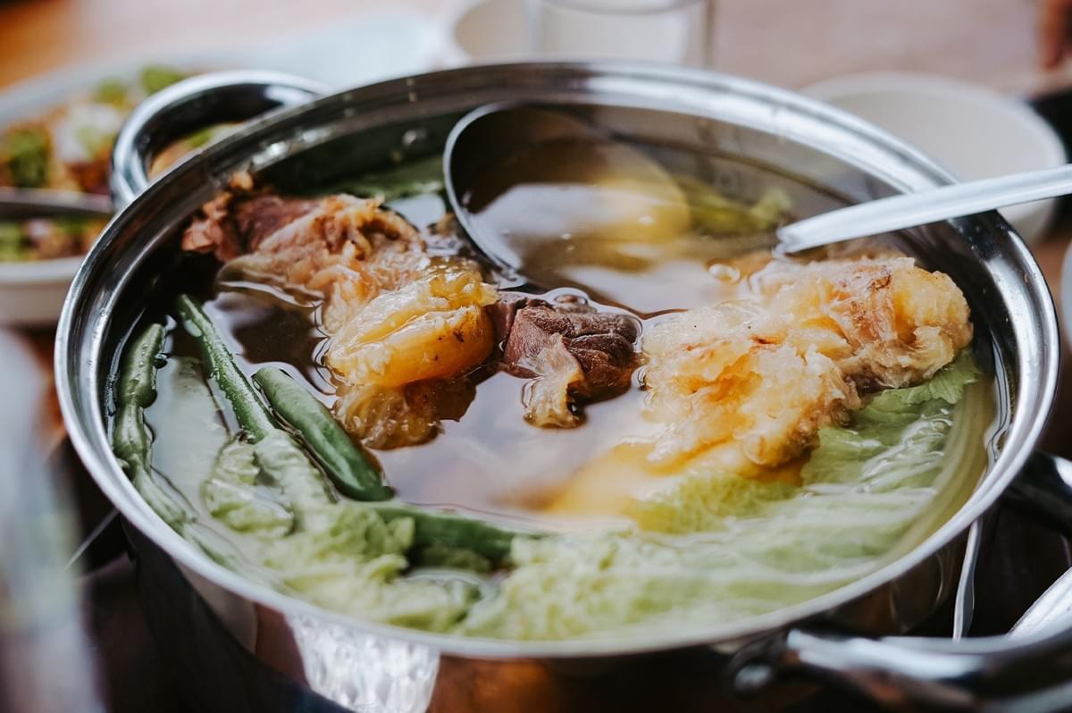 Steamboat hot pot dish featuring broth, meat, and vegetables in a metal pot. Steamboat hot pot dish featuring broth, meat, and vegetables in a metal pot.