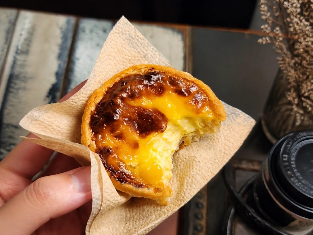 Hand holding a partially eaten Portuguese egg tart wrapped in a napkin. Hand holding a partially eaten Portuguese egg tart wrapped in a napkin.