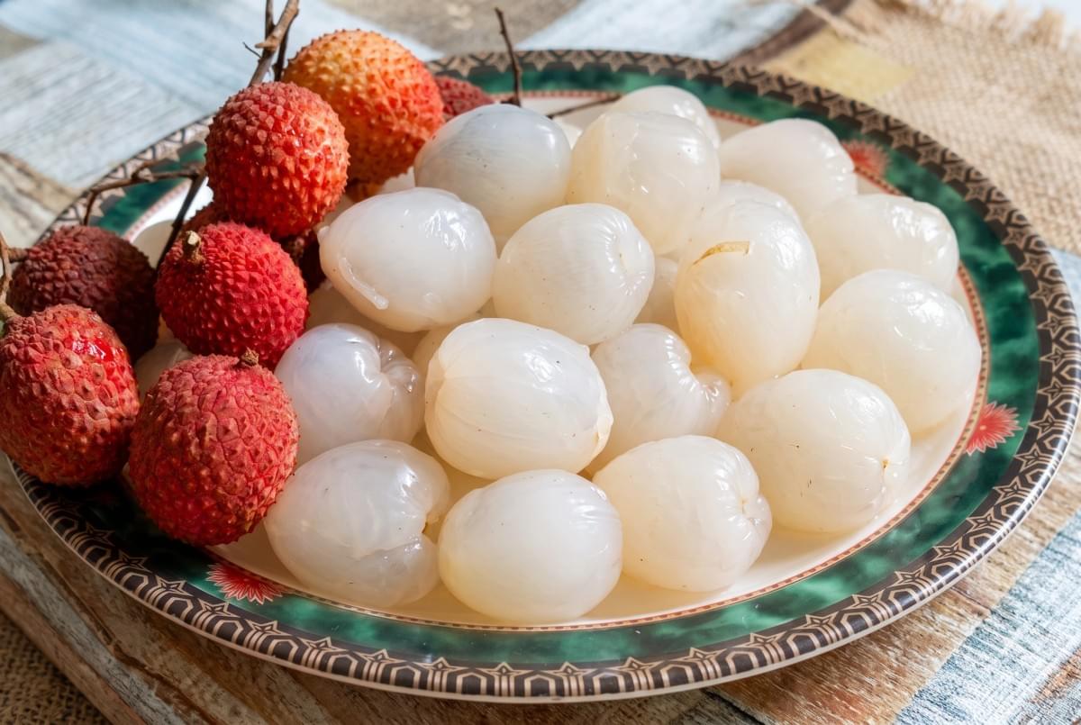 Plate containing whole red lychees and a pile of peeled lychee fruits. Plate containing whole red lychees and a pile of peeled lychee fruits.