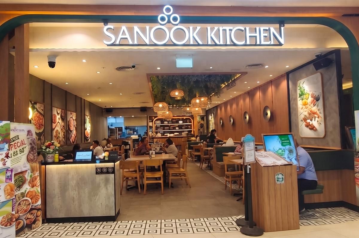 Storefront of the Sanook Kitchen restaurant with a lit sign and indoor dining area. Storefront of the Sanook Kitchen restaurant with a lit sign and indoor dining area.